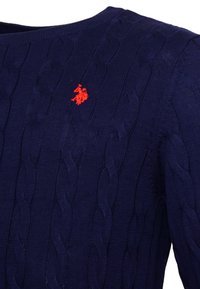 Navy blue knitted sweater with cable pattern and a round neckline, featuring a small red logo on the chest. Textured material.