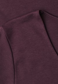 Gros plan sur un tissu en coton violet foncé plié avec un détail de couture visible le long du bord.