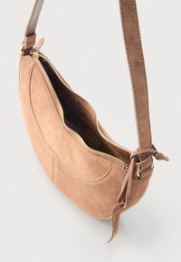 Τσαντάκι χιαστί από καφέ σουέτ με καμπυλωτό σχήμα, χρυστό φερμουάρ και δεμένο διακοσμητικό στο λουρί. Εσωτερικό ορατό, αποκαλύπτοντας λεπτομέρειες τσέπης.