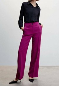 Fuchsia wijde broek met een hoge taille, verticale naden en zijzakken, gecombineerd met een zwarte blouse met kraag en puntige zwarte schoenen.