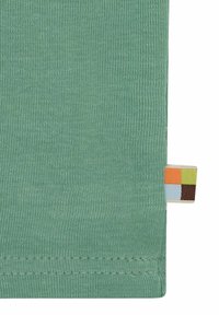 Grüner Strickstoff mit glatter Textur. Verfügt über ein Etikett mit bunten Quadraten in Orange, Blau, Grün und Braun, das am Rand genäht ist.