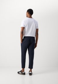 Witte T-shirt met korte mouwen, gecombineerd met marineblauwe elastische broek en zwarte sneakers, met drie witte strepen en een gestructureerde stof.