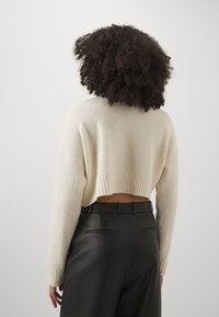 Cream-colored cropped sweater with textured fabric and ribbed hem, paired with black leather pants featuring back pockets.