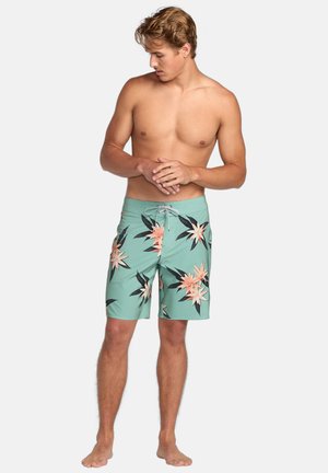 Shorts de bain pour hommes en vert menthe avec un motif floral comportant des fleurs de pêche et des feuilles noires. Le matériau semble léger et à séchage rapide.