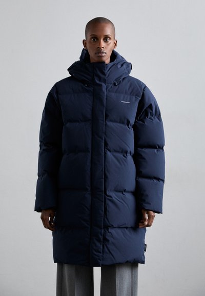 Mørkeblå dunjakke med hætte, med et quiltet design, frontknapper og et logo på brystet. Materialet ser glat og isoleret ud.