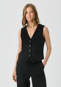 Black pinstriped vest with a v-neckline, sleeveless design, and five-button closure. Features two front pockets and a tailored fit.