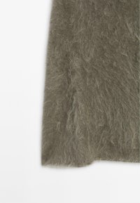 Maglione verde fuzzy con una texture morbida, caratterizzato da una vestibilità comoda e bordi leggermente sfilacciati. Il materiale appare caldo e accogliente.