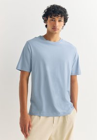 Hele sinine lühikeste varrukatega T-särk, mis on valmistatud puuvillast. Omaduseks on sile tekstuur ja ümmargune kaelus. Lihtne disain ilma mustrite või kaunistusteta.