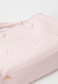 Bolsa texturizada em rosa com o logótipo "VALENTINO" em relevo, metais dourados e alças duplas. Apresenta um formato retangular e um design discreto.