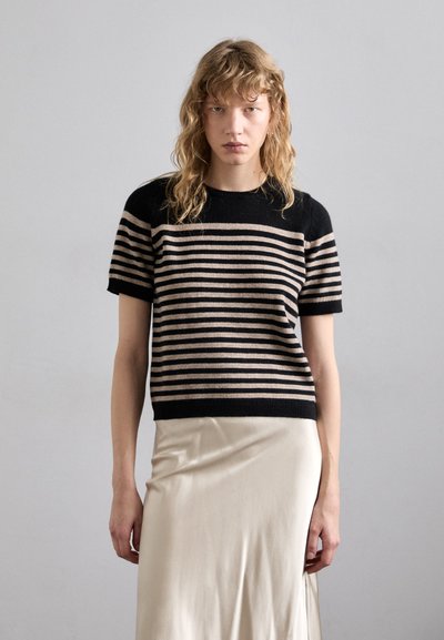 Pull en tricot à rayures noires et beiges à manches courtes, avec un col rond, associé à une jupe midi en crêpe de couleur crème, lisse et satinée.