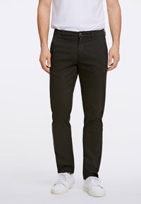 Pantaloni neri in cotone con vestibilità dritta, tasche anteriori, chiusura con bottone e una leggera lucentezza, abbinati a sneakers bianche.