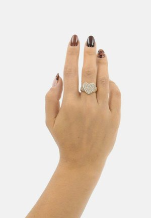 Hand mit braunen und Leopardenmuster-Nägeln, die einen goldenen, herzförmigen Ring mit kleinen Diamanten am Mittelfinger trägt.