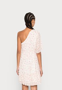 Jedno-ramienna sukienka z przezroczystego białego materiału, ozdobiona małymi różowymi i zielonymi wzorami kwiatowymi, z rozkloszowanym dołem i marszczoną talią.