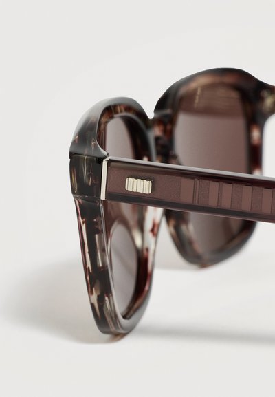 Lunettes de soleil à motif écailles de tortue marron avec verres foncés, montrant un design détaillé de la charnière et des branches sur fond blanc.