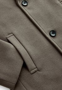 Cappotto di lana marrone con una texture morbida, caratterizzato da colli rotondi, due chiusure a bottoni neri e tasche laterali.
