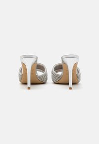 Chaussures à talons aiguilles argentées avec une finition métallique lisse et un tissu argenté texturé sur les côtés. Design à dos ouvert et bout pointu.