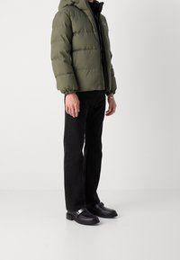 Puffjacka i olivgrön med huva, dragkedjestängning och elastiska ärmslut. Kombinerad med svarta raka jeans och svarta slip-on-skor.