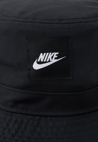 Czarna czapka typu bucket z wyszywaną kwadratową łatą z białym logo Nike oraz charakterystycznym swooshem na środku przodu.