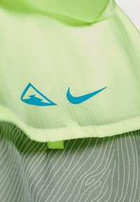 Lysegrønt stof med et gittermønster, der har en blå lyn-logo og en blå Nike swoosh. Designet har bølgede grå accenter.