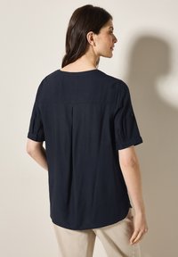 Blusa blu navy a maniche corte, tessuto liscio, leggero lucido, dettaglio con piega sul retro, orlo arrotondato, maniche arrotolate con dettagli in bottone.