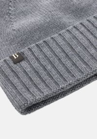 Gorro de tricot gris con borde acanalado y una pequeña etiqueta negra con un logo blanco de la letra "B". La textura es suave y gruesa.