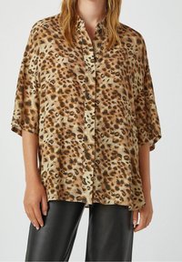 Braun und beige Leopardenmuster Kurzarmhemd mit loser Passform. Der Stoff hat eine glatte, leichte Textur.