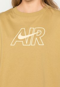 Beige bomullströja med rund halsringning som har en stor vit "AIR" logotyp tillsammans med en Nike swoosh, mjukt material och avslappnad passform.