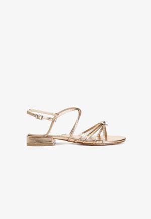 Kultakylkiset sandaalit, joissa on pieni tukijalka, useita hoikkia hihnoja ja koristeelliset kivisomisteet edessä. Säädettävä nilkkahihna.