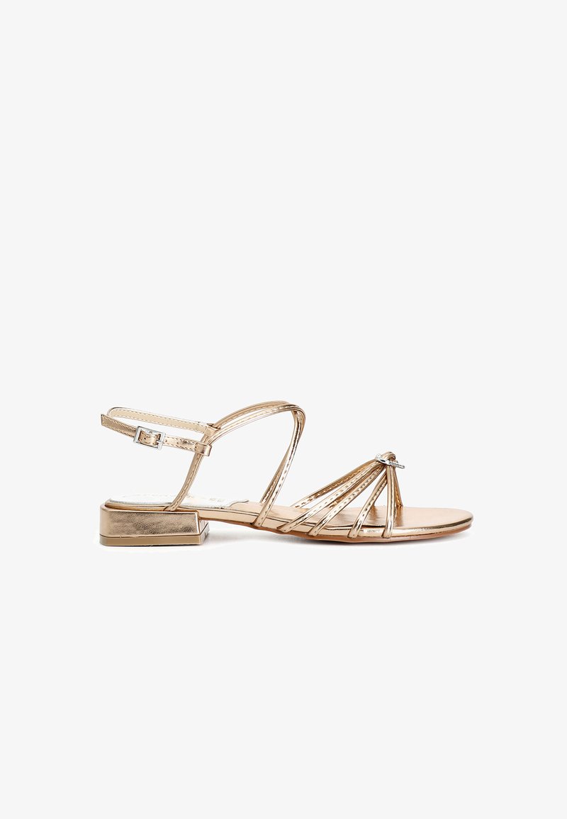 Kultakylkiset sandaalit, joissa on pieni tukijalka, useita hoikkia hihnoja ja koristeelliset kivisomisteet edessä. Säädettävä nilkkahihna.