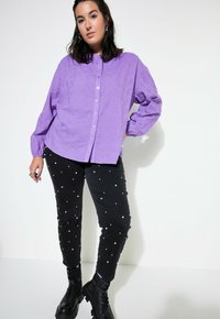 Camicia a maniche lunghe viola con un motivo testurizzato, chiusura a bottoni. Pantaloni neri con dettagli in perle bianche. Stivali neri chunky.