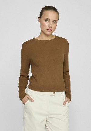 Pull en maille côtelée marron avec des manches longues et un col rond, associé à un pantalon de couleur claire. Design et texture simples.