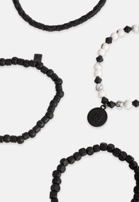 Penki apyrankės, įskaitant pintą juodos odos apyrankę, tris juodai baltų karoliukų dizainus su skirtingomis formomis ir apvalią medalinę akcentą.