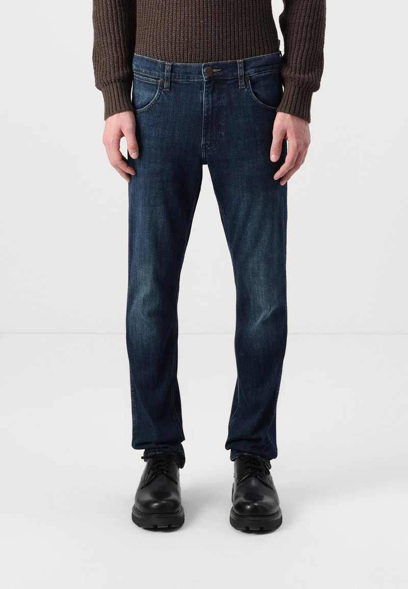 Donkerblauwe denim jeans met een rechte pasvorm, voorzien van vijf zakken, een knoopsluiting en subtiele vervaging op de dijen.