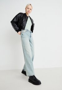 Černá kožená bomber bunda přes světle zelený top, v kombinaci se světle modrými rovnými džíny a černými platformovými botami. Minimalistický design.