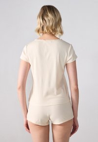 Kremasta rebrasta tkanina loungewear set, ki vključuje kratkosleeven top z nabranim izrezom in ujemajoče se kratke hlače s pomočnim elastičnim pasom.