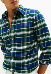 Camisa de franela a cuadros que presenta una combinación de colores azul, verde y blanco con acentos amarillos, cierre de botones y un bolsillo en el pecho.