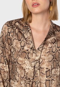 Blusa a stampa rettile marrone con scollo a V, tessuto testurizzato e vestibilità ampia. Presenta diverse tonalità di marrone e nero nel motivo.