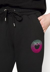 Czarne dresy z paskiem ściągającym w talii, kieszenią boczną oraz kolorową okrągłą grafiką w różu i turkusie na lewym udzie.