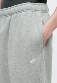 Γκρι παντελόνι φόρμας Nike με ελαστική μέση, πλαϊνές τσέπες και μικρό λευκό λογότυπο. Μαλακό, υφασμένο ύφασμα.