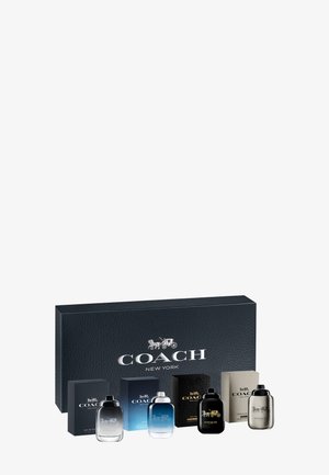 Zestaw czterech flakonów perfum Coach New York wraz z dopasowanymi pudełkami w kolorach czarnym, niebieskim i beżowym, ustawionych przed dużym czarnym pudełkiem.