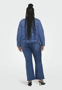 Denim jakna v srednje modri barvi s klasičnim krojem, okrašena s srebrnimi zakovicami na rokavih, v kombinaciji s širšimi hlačami in črnimi visokimi petami.