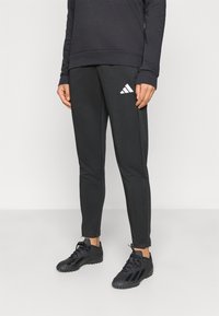 Μαύρο αθλητικό παντελόνι από λείο ύφασμα, με στενά πόδια, ελαστική μέση και λευκό λογότυπο Adidas στην αριστερή πλευρά.