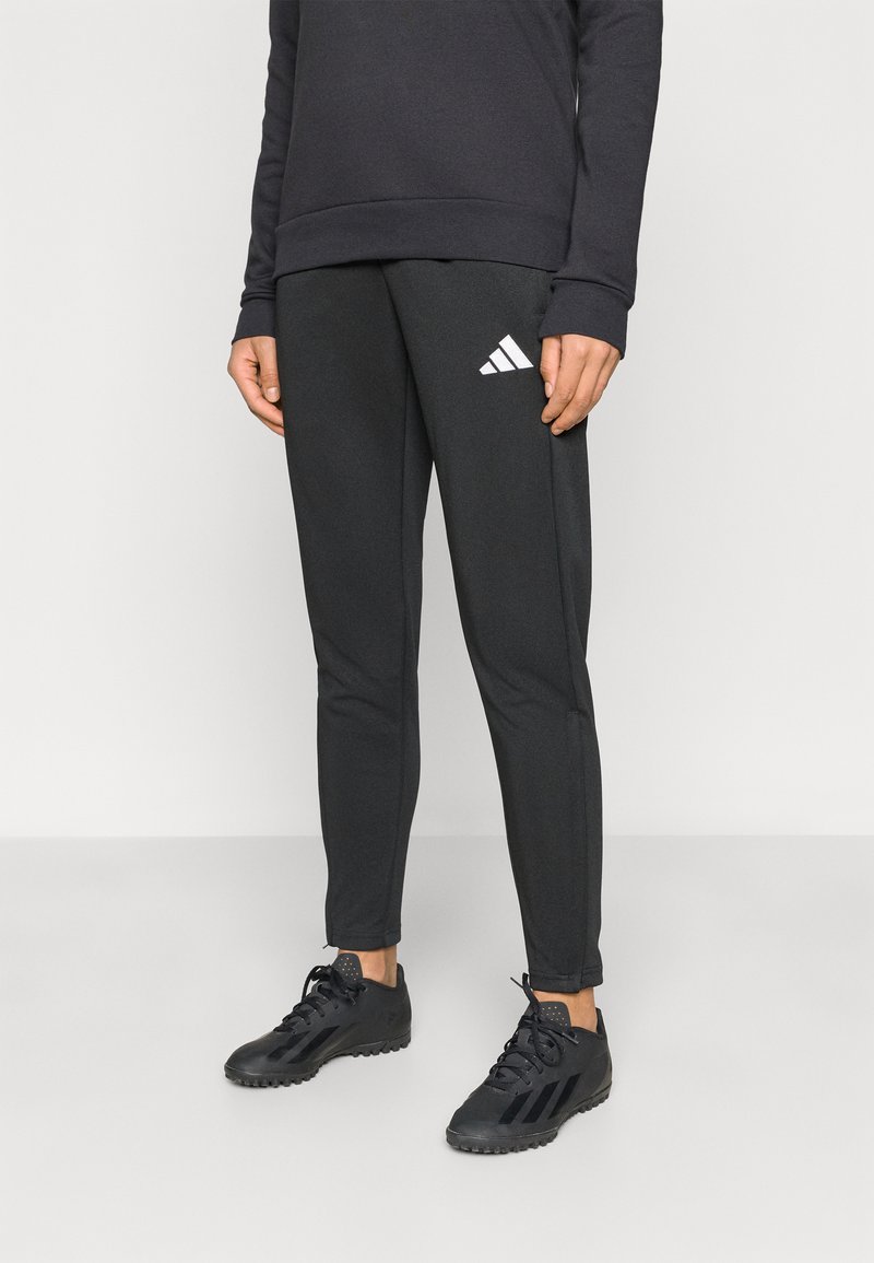 Μαύρο αθλητικό παντελόνι από λείο ύφασμα, με στενά πόδια, ελαστική μέση και λευκό λογότυπο Adidas στην αριστερή πλευρά.
