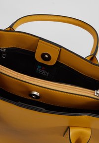 Borsa a spalla in pelle gialla con texture e bordi neri. Presenta una chiusura a scatto magnetico, una tasca interna con zip e un'etichetta di marca.
