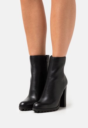 Zwarte leren enkellaarsjes met een ronde neus, stevige blokhak en ritssluiting aan de zijkant. Gladde textuur met geribbelde rubberen buitenzool voor grip.