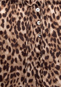 Tkanina s leopardím vzorem v odstínech hnědé a béžové. Na přední straně má pět knoflíků a stahovací pás v pase. Hladká texturu.