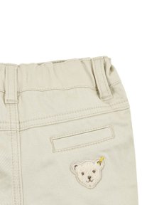 Lichtbeige broek met een elastische tailleband, achterzak en een geweven berengezicht met een gele accenten.