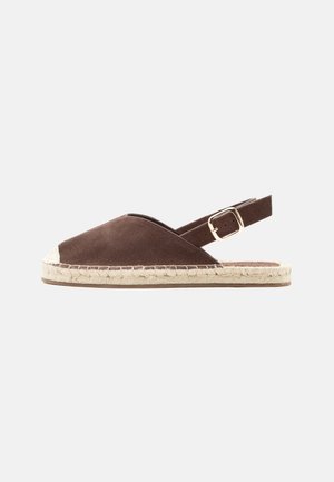 Sandale espadrille en daim marron avec semelle en jute et bride arrière réglable avec boucle dorée, présentée sur un fond gris clair uni.