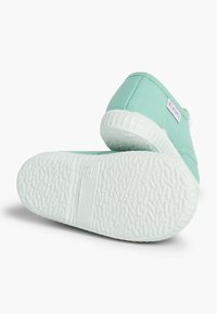 Scarpe slip-on in tela verde menta con una suola in gomma bianca testurizzata, dotate di un piccolo tag con logo sul lato e un design della punta arrotondato.