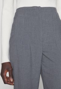 Grijze hooggebande broeken van textiel met scherpe plooien en zijzakken, gecombineerd met een geribbelde witte trui.